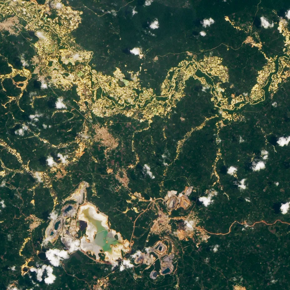 O imagine satelitară în culori naturale a unei păduri din Ghana, cu cicatrici miniere palide, aurii și bej, drumuri și cariere deschise răspândite în peisaj.